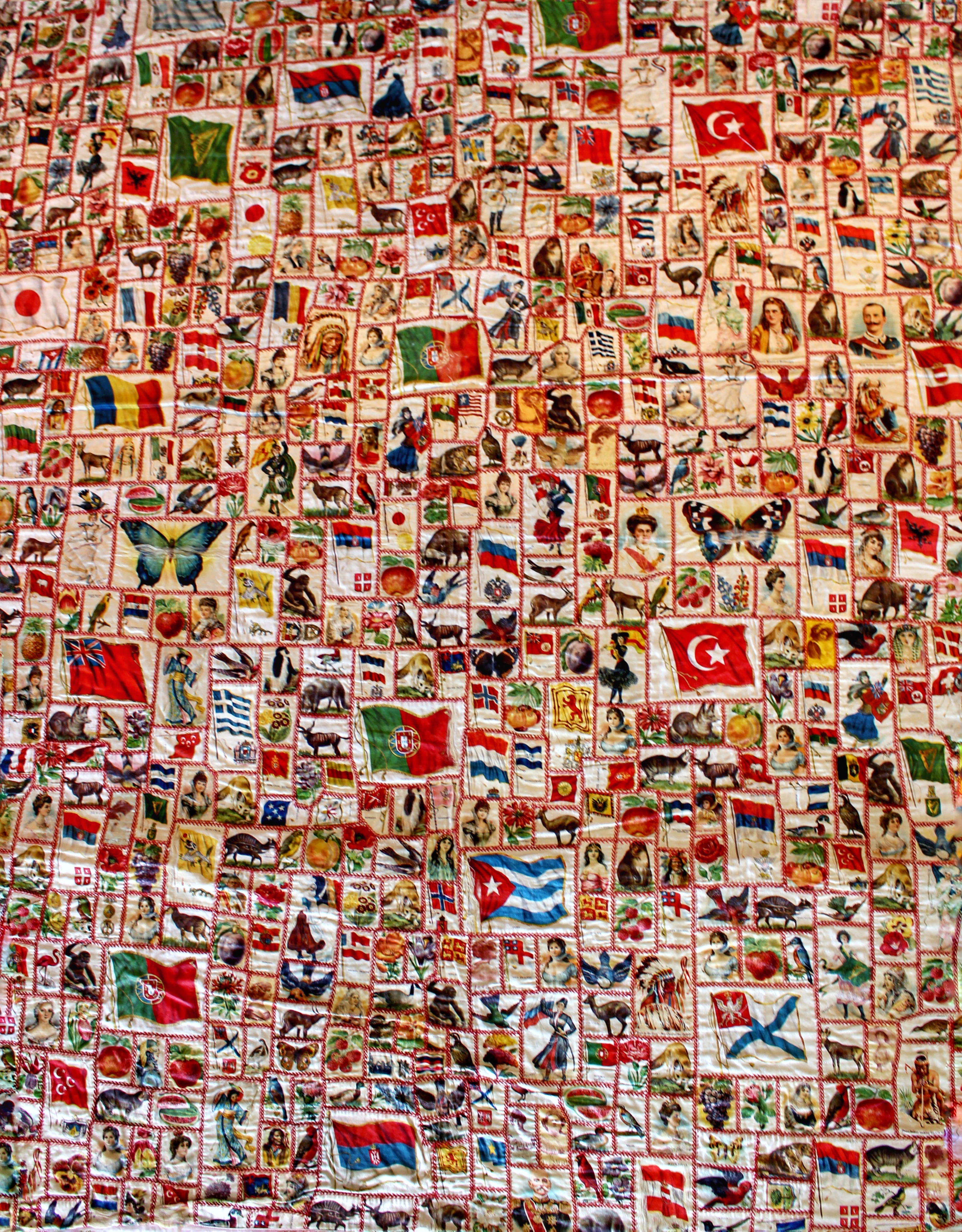 section of quilt made of cigarette silks pieced together showing flags of the world, important figures, plants and animals