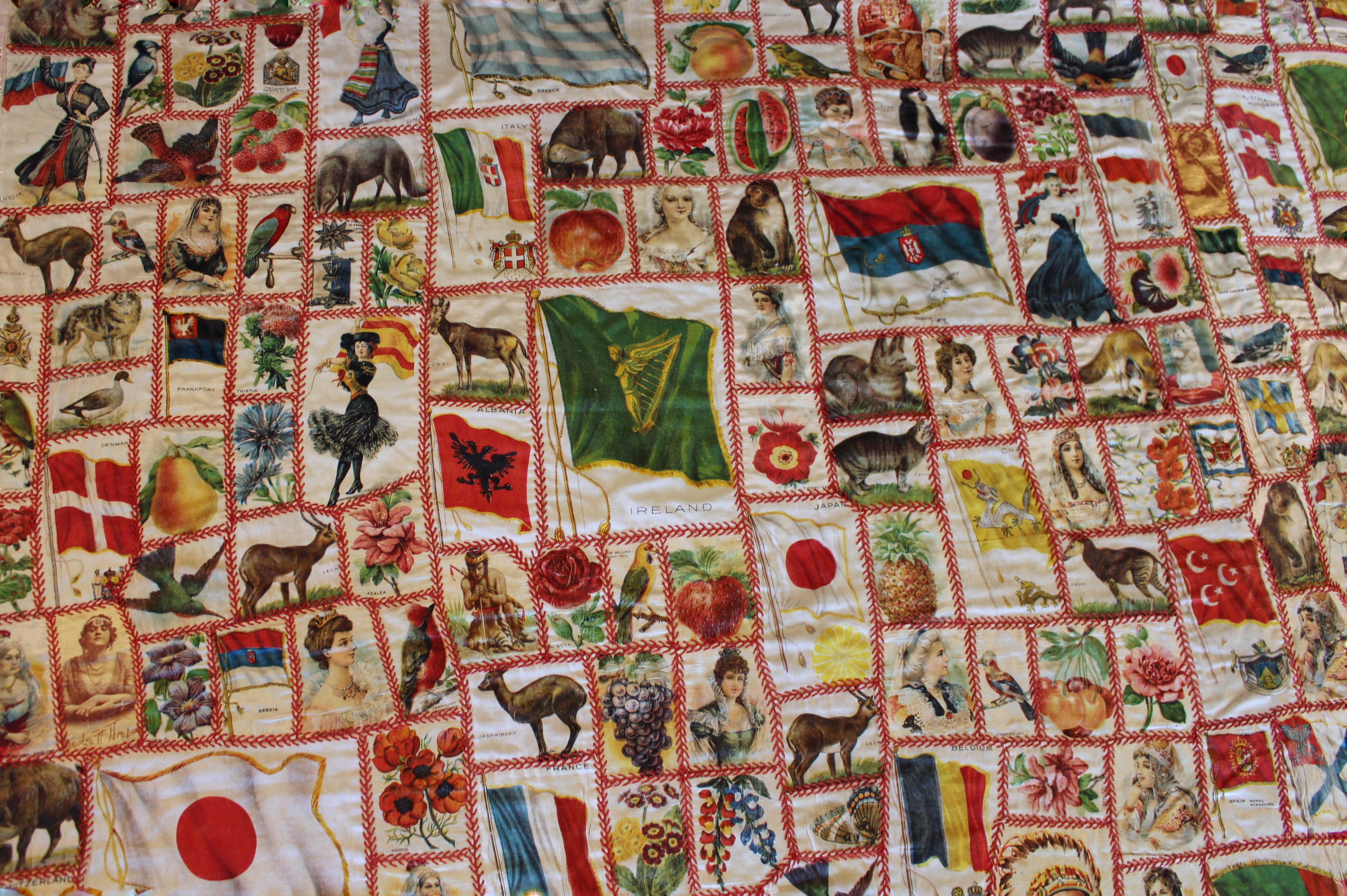 section of quilt made of cigarette silks pieced together showing flags of the world, important figures, plants and animals