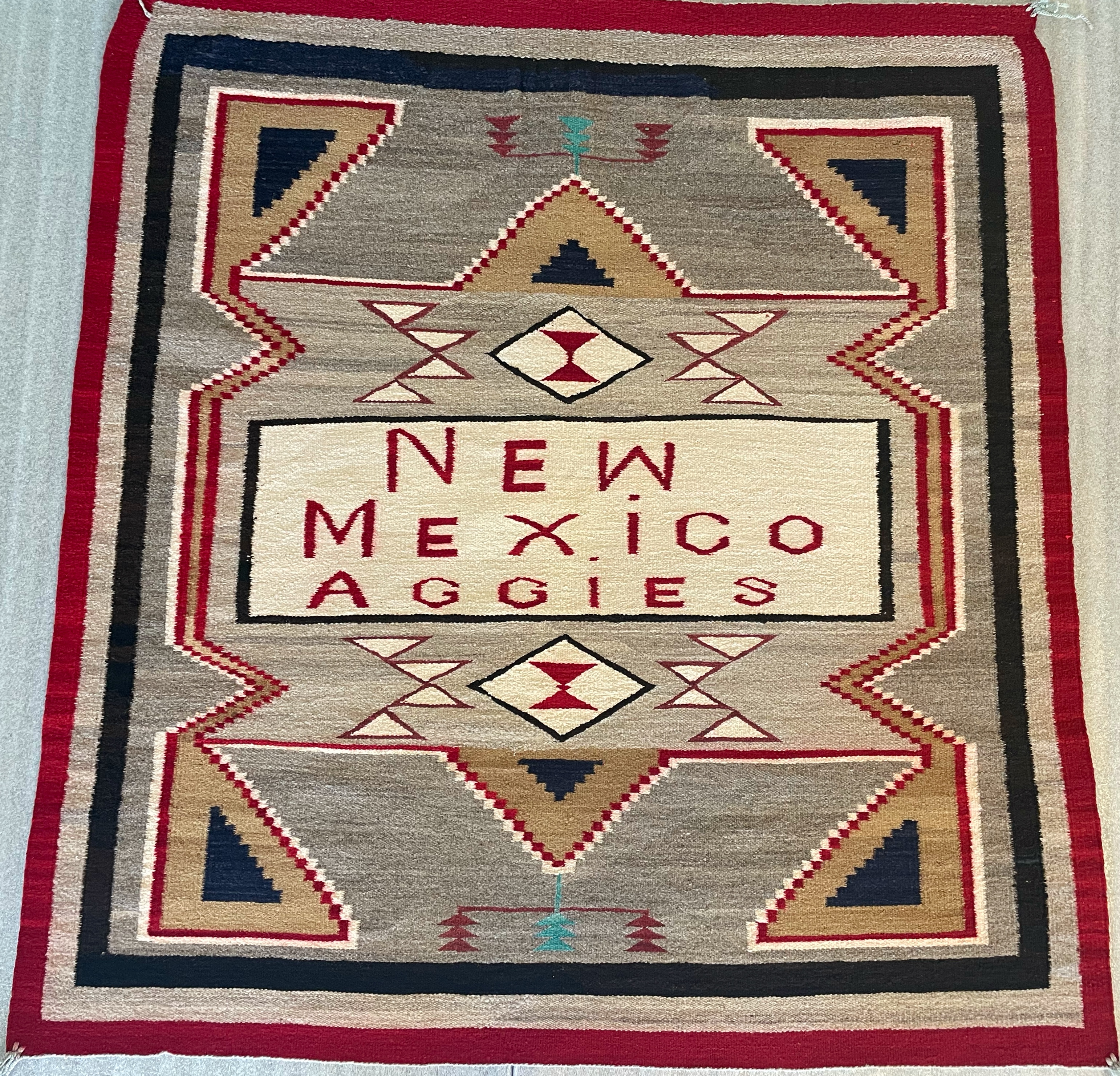 Brown woven rug featuring white, tan, black, and red geometric designs and New Mexico Aggies at the center.