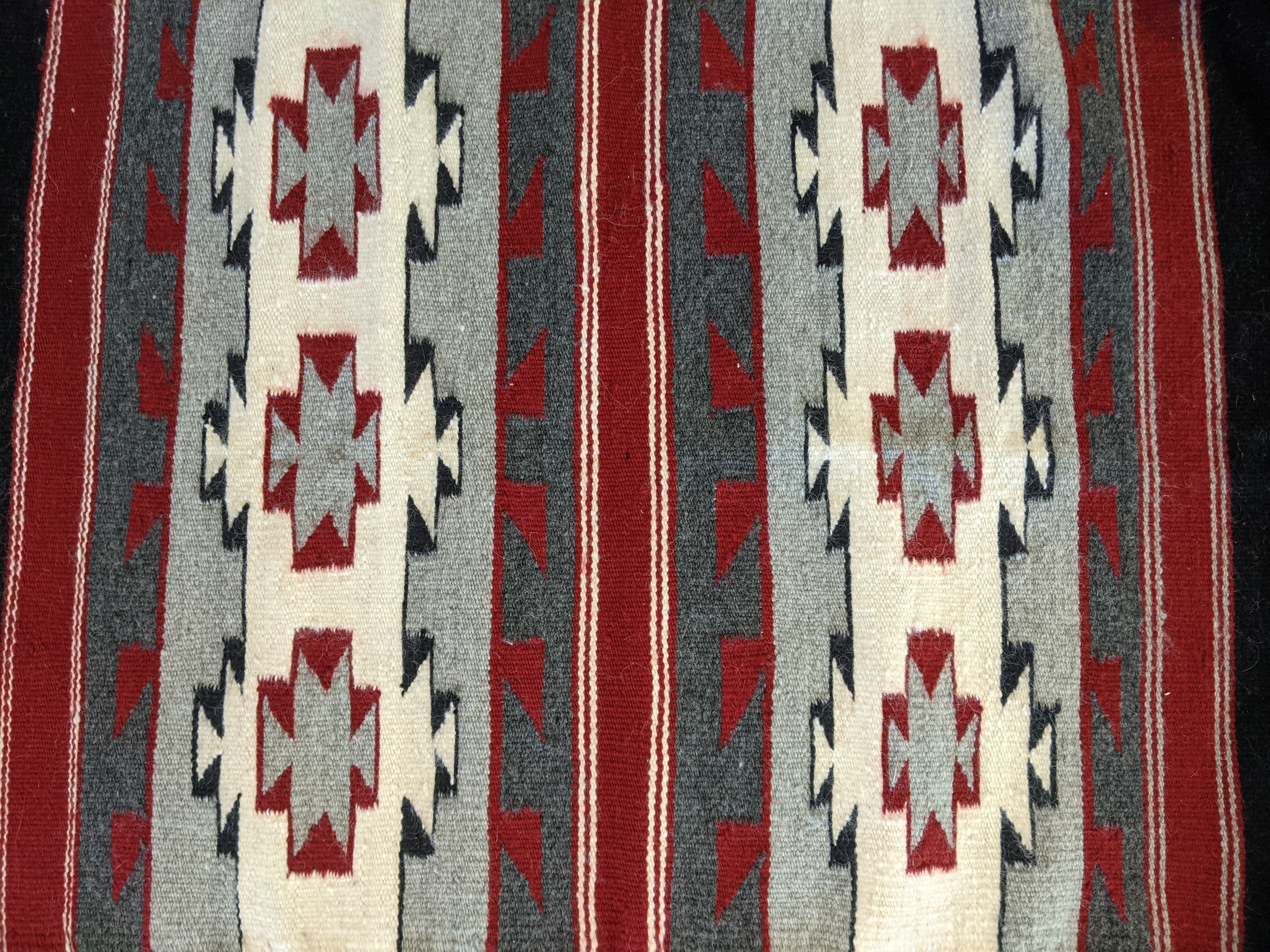 Detail of rug with red, white, gray, and black stripes and geometric patterns